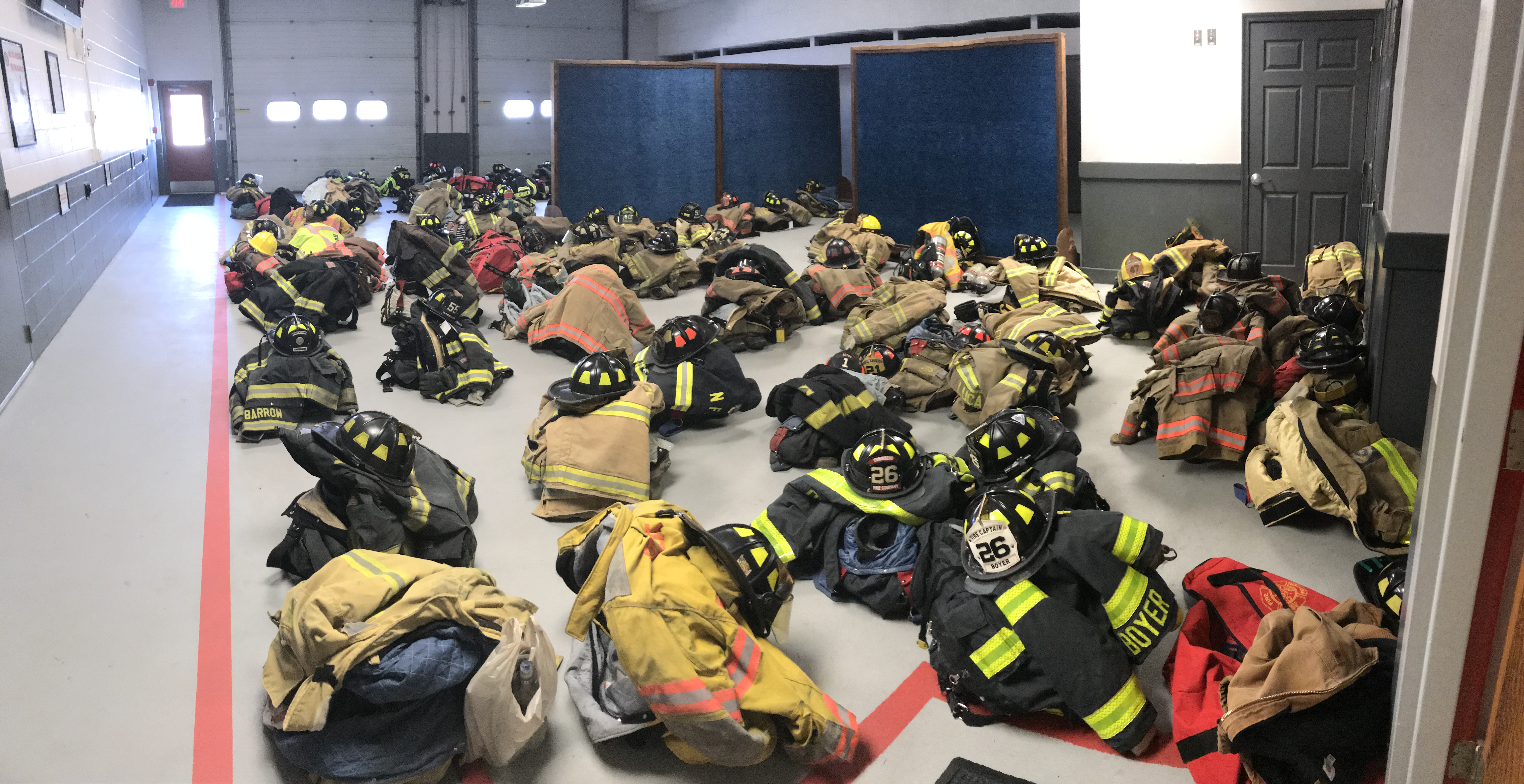 Photo of firefighters uniforms from different fire companies spread-out across the floor with helmets inside a building